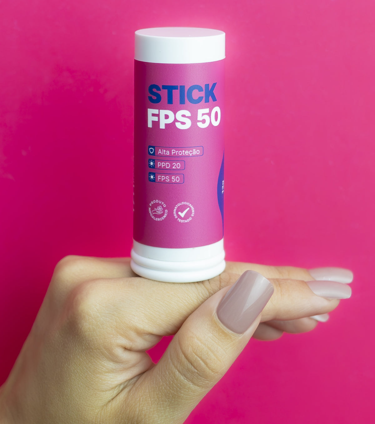 Mão segurando o Stick FPS 50 Peak Beauty sobre fundo rosa
